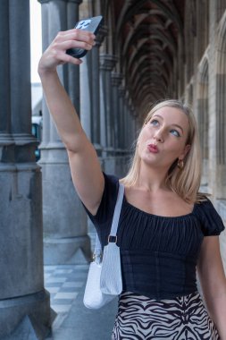 Parlak makyajlı, Avrupa 'da güzel bir günde enerjisini ifade eden harika bir beyaz kadın modelin yüksek kaliteli portresi. Şık giyinmiş güzel sarışın kadın, selfie çekerken...