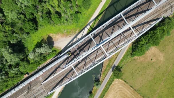 从空中俯瞰 一列火车穿过一座金属铁路桥 在河水之上 森林和田野在一边 从无人侦察机俯瞰铁路 比利时 高质量的4K镜头 — 图库视频影像