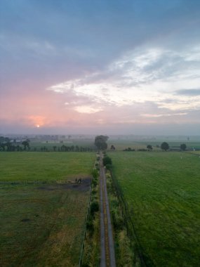 Sise giden dolambaçlı bir kır yolunun merkez odak noktasını oluşturduğu yaz manzarasının nefes kesici bir görüntüsü. Dramatik bir gün batımına karşı çekilen fotoğraf ruhani bir ahenk yaratır.