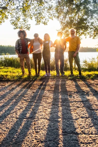 The shadows of multiracial young friends admiring the golden sunset and having fun at the side of forest lake. Lifestyle concept of friendship and fun. High quality photo