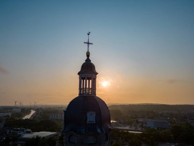 Sakin bir sabahın ruhani güzelliğini bu nefes kesici hava fotoğrafıyla yakala. Bir kilise kulesinin silueti, parlak bir gün doğumunun zeminine karşı dimdik ayakta duruyor. Umudu ve huzuru simgeliyor.