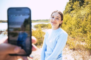 Bu fotoğrafta paylaşılan bir anın sihrine tanık olun. Bir adamın eli, güzel ve neşeli beyaz kız arkadaşının yaz tatilinde bir fotoğrafını sevgiyle yakalar.