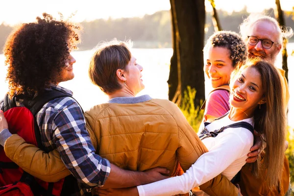 Celebrate the richness of diversity and the magic of natures canvas in this captivating scene. A multiracial group of young people with backpacks stand close, sharing an embrace while admiring the