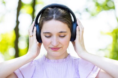 Doğanın huzuru içinde müzik dünyasına dalmış genç bir kadının dingin güzelliğini keşfedin. Kulaklıkları düzgün, gözleri de derin bir konsantrasyonda.