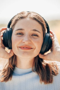 Müzik dünyasına dalmış güzel ve çekici genç bir kadının büyüleyici görüntüsünü deneyimleyin. Kablosuz kulaklıklar sayesinde. Onun huzurlu yüzü doğanın saf neşesini yansıtıyor.