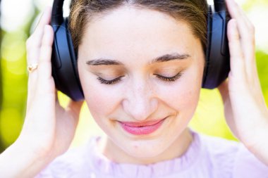 Doğanın huzuru içinde müzik dünyasına dalmış genç bir kadının dingin güzelliğini keşfedin. Kulaklıkları düzgün, gözleri de derin bir konsantrasyonda.