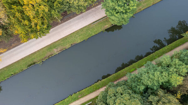 This mesmerizing aerial perspective offers a top-down view of a peaceful canal winding its way through a lush, green landscape. Towering trees line the waters edge, creating a picturesque scene of