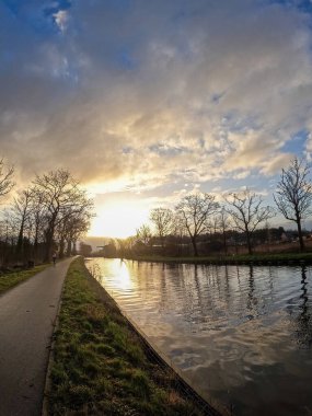 Güneş sakin bir kış kanalı üzerinde batarken doğa draması yaşanıyor. Gökyüzünü turuncu, pembe ve morumsu renklerle boyuyor. Kış Kanalı Günbatımı. Yüksek kalite fotoğraf