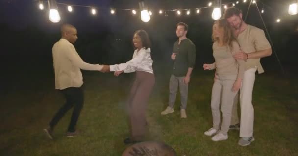 在一个迷人的花园灯光下 在一个烧烤晚会上 一群来自不同种族背景 风格和舞蹈的多姿多彩的千禧年好友 组成了一个生气勃勃 欢乐的团队 多种族 — 图库视频影像