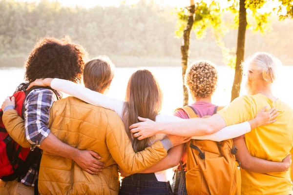 A multiethnic group of friends, bound by love and adventure, stand united by a forest lake. As the sun casts a golden farewell, their close embrace mirrors the days warm memories. Their backpacks tell
