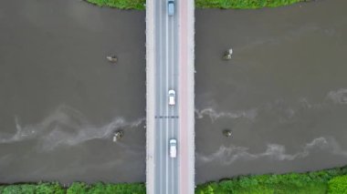 Zaman ve uzayda asılı kalan bir dron gözü, köprüden geçen sürekli araç akışını kaydeder. Aşağıdaki nehir kendi hızında ilerliyor, yukarıdaki insan koşuşturmasına aldırış etmeden. Bu yukarıdan aşağıya görünüm