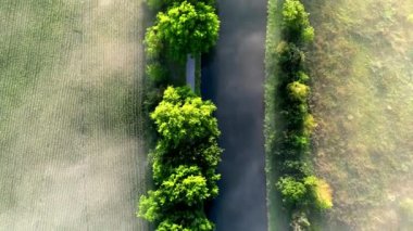Yukarıda, drone mercekleri kırsal güzelliğin sakin bir sahnesini gözler önüne seriyor. Yukarıdaki gökyüzünü yansıtan bir kanal, manzaranın içinde süzülüyor, etrafını düzenli olarak çevreleyen ağaçlar akışının koruyucuları olarak duruyorlar.
