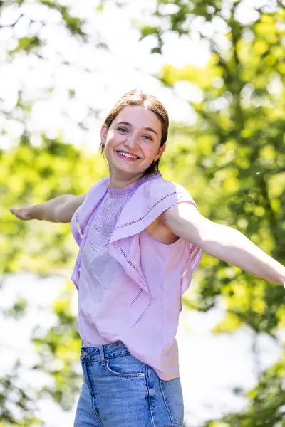 Stock image In a peaceful forest, a young woman stands side-on, her arms outstretched, embracing the warm, sunlit day. Surrounded by trees, she embodies a spirit of freedom and joy, deeply connected to the