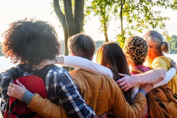 На этой фотографии изображены пять молодых, многорасовых друзей, которые празднуют восхождение на вершину у берегов лесного озера. Купаясь в лучах заходящего солнца