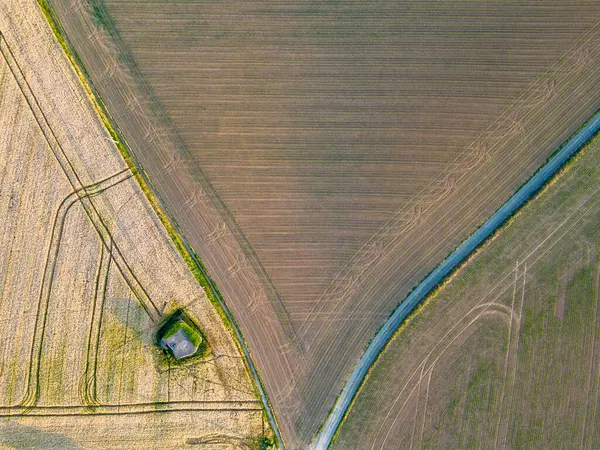 This image from above captures the geometric beauty of farmland, with its various shades of brown and green creating a patchwork quilt of agricultural land. A sinuous blue waterway carves through the