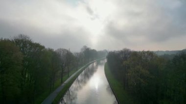 Bu hareketli görüntüde, bir kanal boyunca ilerliyoruz, bulutların arasından parlayan güneşe doğru ilerliyoruz. Su yolu aydınlanmanın tam kalbine giden yol gösterici bir hat görevi görür.