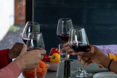 Kadeh kaldırma anını kırmızı şarap kadehiyle yakalayan samimi ve samimi bir sahne. Ellere ve gözlüklere odaklanmış durumda, bu da arkadaşlar arasında sıkı sıkıya bağlı bir ortam olduğunu gösteriyor. Bulanık arkaplan