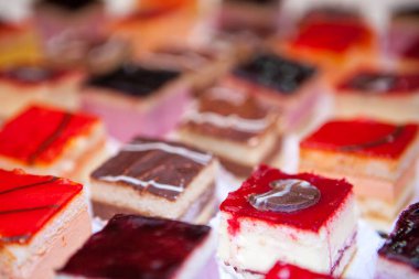 Görüntü canlı ve iştah açıcı, her biri titizlikle hazırlanmış ve sunulmuş çeşitli minik dörtlülerden oluşuyor. Küçük kekler parlak, renkli camlarla kaplıdır, bazıları berrak ve pırıl pırıldır.