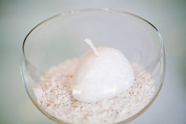 Bu resim, cam bir kase içinde narin kristallerden oluşan bir yatakta tek bir beyaz mumun bulunduğu minimalist ama huzurlu bir süs eşyası yakalıyor. Yumuşak odaklı arka plan vurgu yapar