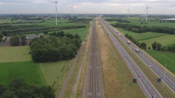 この画像は 地平線に対して背の高い風力タービンに囲まれた高速道路のまっすぐなストレッチの空中視点を提供しています 再生可能エネルギーと輸送の並列化 — ストック動画