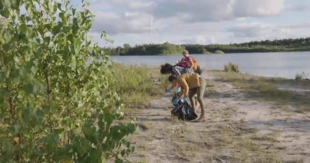 この感動的な映像は 若いボランティアのグループをキャプチャし 多様な外観と目的で団結し 湖畔の清掃活動に参加します 手袋およびゴミ袋が装備されている それら — ストック動画