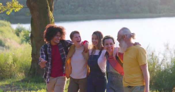 这张充满活力的图片捕捉了一群年龄和背景各异的朋友 他们在湖边自发地展示了自己的笑声和爱心 阳光温暖的光芒穿透了整个场景 — 图库视频影像