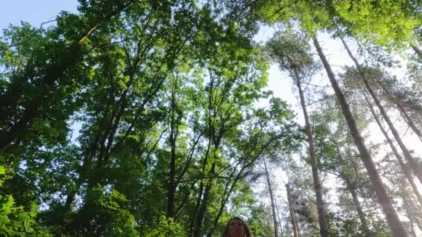 地上から捉えられた映像は ピンクのスポーツ服を着た女性を まるで 活気に満ちた森のタワーに囲まれた緑の木に囲まれているかのように描いています アングルが示唆する — ストック動画