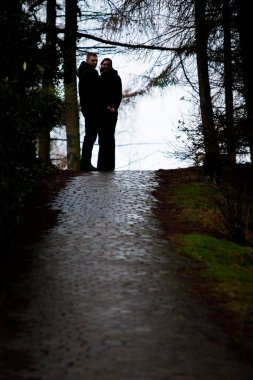Bu resimde, bir çift birbirine yakın duruyor, nemli bir yolda, huzurlu bir ormanın içinden sisli bir göle doğru giden bir anı paylaşıyorlar. Çiftin siluetleri doğal olarak çerçevelenmiştir.