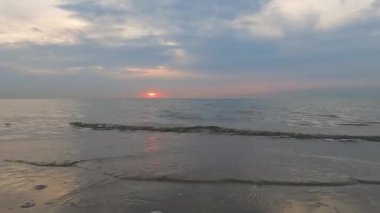 Bu görüntüler, sakin bir okyanusun ufkunun altında güneşlerin son kez battığı deniz kıyısındaki bir günün barışçıl sonunu özetliyor. Pastel gökyüzü, su yüzeyine yansıyor.