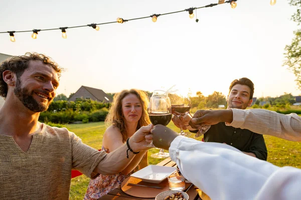 In the golden light of the setting sun, a group of friends raises their wine glasses for a toast. A man with a beaming smile is at the center, surrounded by friends who are equally enjoying the moment