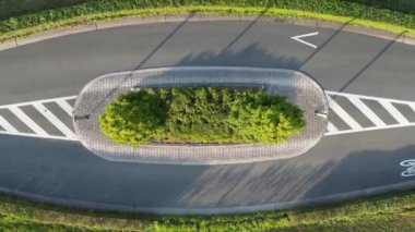 Bu İHA görüntüsü, şehirli asfalt yollarının ortasındaki bereketli ağaçlarla bezenmiş bir trafik adasına eşsiz bir tepeden tırnağa bakış açısı sağlıyor. Doğanın yeşilliğe karşı kontrastı