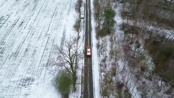 这个迷人的无人驾驶飞机镜头展示了一辆单独的橙色车穿过白雪覆盖的乡间道路 旁边是光秃秃的冬季树木和田野 鸟瞰全景凸显了 — 图库视频影像