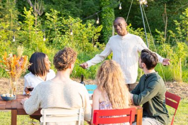 Akşamları ev sahibi, siyah bir adam, kollarını açmış, açık hava toplantılarında sıcak bir karşılama jesti yapıyor. Siyahi bir kadın, beyaz bir kadın ve beyaz bir erkek de dahil olmak üzere oturma izni almış konuklarımız...