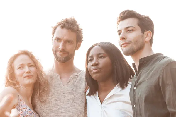 n the tender glow of the afternoon sun, a diverse group of friends stands close together, embodying the spirit of unity. The photograph captures a Caucasian man and woman, a Black woman, and a Middle
