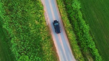 Gökyüzünden çekilen bu görüntüler, kıvrımlı kırsal bir yolda gezinen bir arabanın canlı yeşil yapraklarla kaplı olduğunu gösteriyor. Yukarıdan aşağı görünüm araçlar arasında hareket ederken pürüzsüzlüğü vurgular