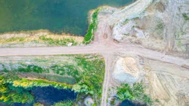 Bu hava görüntüsü, canlı bitki örtüsüne sahip doğal bir su kütlesi ile kazı ve inşaat faaliyetleri tarafından bozulan bitişik arazi arasında katı bir tezat oluşturuyor. Görüntü görüntüyü yakalar
