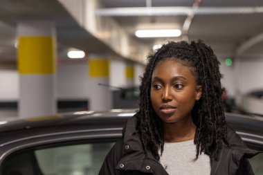 Şehrin otoparkının bastırılmış ışıklarında genç bir siyahi kadın dinlenme anında yakalanır. Bakışları kameradan uzağa çevrilmiş, düşünce ya da gözlemlerde kaybolmuş. Öyle.