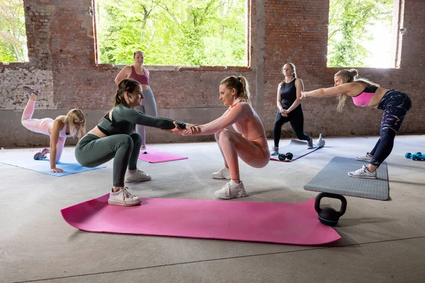 stock image In this dynamic scene, a group of women participates in a varied fitness routine within a spacious, industrial-style workout area. The central focus is on two women engaging in a partner squat