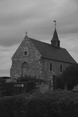 Bu monokromatik görüntü Cap-Blanc-Nez yakınlarındaki bir köyde bulunan eski bir taş şapeli gösteriyor. Kararmış taş cephesi ve geleneksel mimarisi bulutlu gökyüzüne karşı sert bir şekilde özetlenmiştir.