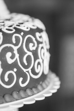 Bu siyah ve beyaz resim, bir kekin üzerindeki beyaz kremanın karmaşık girdaplarını ustalıkla yakalıyor. Yakından bakıldığında, borulama tekniği tarafından oluşturulan desenler ve dokular vurgulanıyor.