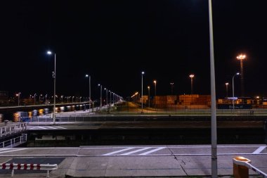 Bu gece görüntüsü Antwerp Limanı 'nın hareketli hareketlerini yakalar. Yapay ışıklar yıldızlar gibi parıldar ve aşağıdaki sakin sulara enerjilerini yansıtır. Rıhtım canlı.