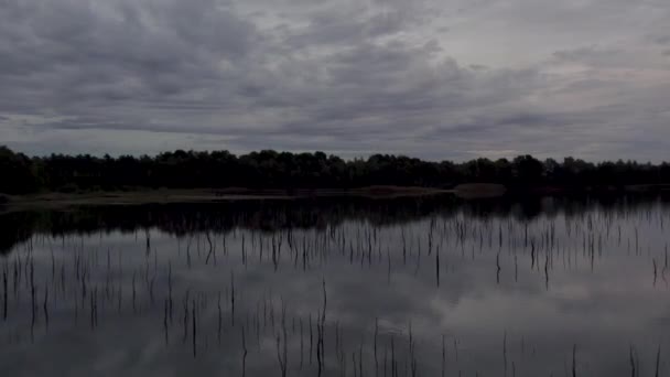 この大気中の無人機の映像は 天空の下の夕暮れのセットとしてムーディー湖を示しています 湖のガラス張りの表面は完全に木のシルエットをしながら 上空の暗い 爆発する雲を反映しています — ストック動画