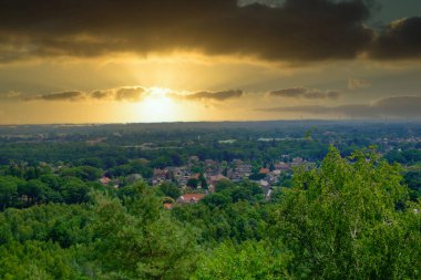 Bu anımsatıcı görüntü batan güneşin altın ışığıyla yıkanan banliyö manzarasının dramatik güzelliğini yakalar. Yoğun bulut örtüsü güneş ışınlarına çarpıcı bir tezat ekler.