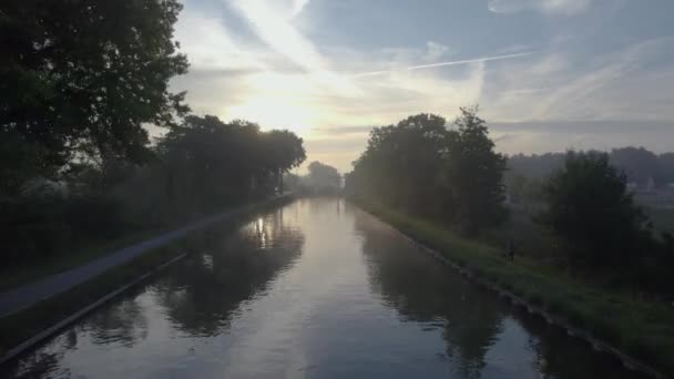 このストック映像は 一日の最初の光が平和な水路を照らすように素朴な朝の本質を捉えています カメラは 隣接する経路の景色を提供し 運河の上をグラフ — ストック動画