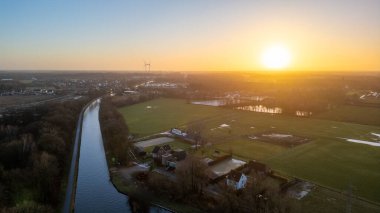 Bu büyüleyici hava manzarası, sakin bir kırsal bölgede gün batımının huzur verici güzelliğini yakalar. Dönen bir nehir, yemyeşil tarlalarda kıvrımlı bir yol açar.