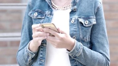 Bu video, kot ceketli bir şahsın akıllı telefonuyla ağır çekimde etkileşime girdiği modern bir bağlantıyı özenle tasvir ediyor. Yavaşlayan hız izleyicilere izin verir