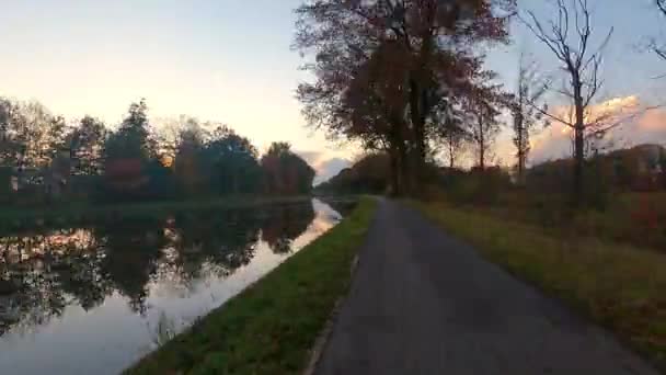 このストック映像で風光明媚な公園を巡る魅惑的なタイムワープの旅を体験してください ビデオは急速に反射する川の横の秋の木が並ぶ道に沿って視聴者を取ります — ストック動画