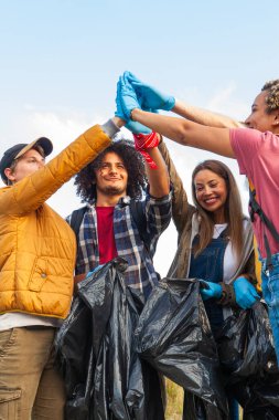 Görüntü, başarılı çevre temizliğini kutlayan bir grup hevesli gönüllüyü gösteriyor. Çeşitli bireylerden oluşan takım, eldivenli eldiveni birlikte kaldırırken görülüyor.