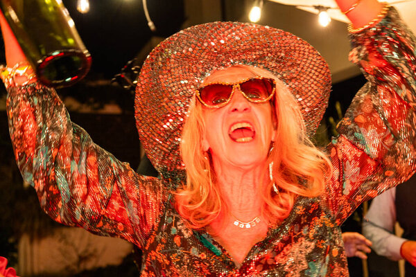 Captured in a moment of sheer ecstasy, this image features a jubilant person caught in the throes of celebration. Clad in a dazzling sequined hat and matching outfit, their face is a portrait of