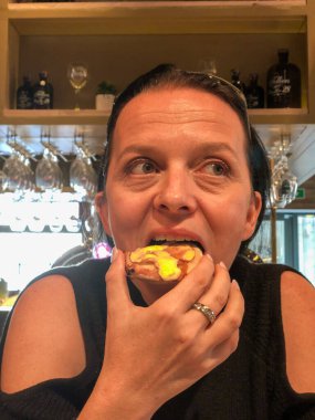 Bu görüntü, kremalı ekinlerden bir ısırık almak üzere olan bir kadının samimi bir anını yakalıyor. İçerde, şarap kadehleri ve şişelerden oluşan bir arka planı var. Bu da ev ortamının rahat olduğunu gösteriyor. Onun.